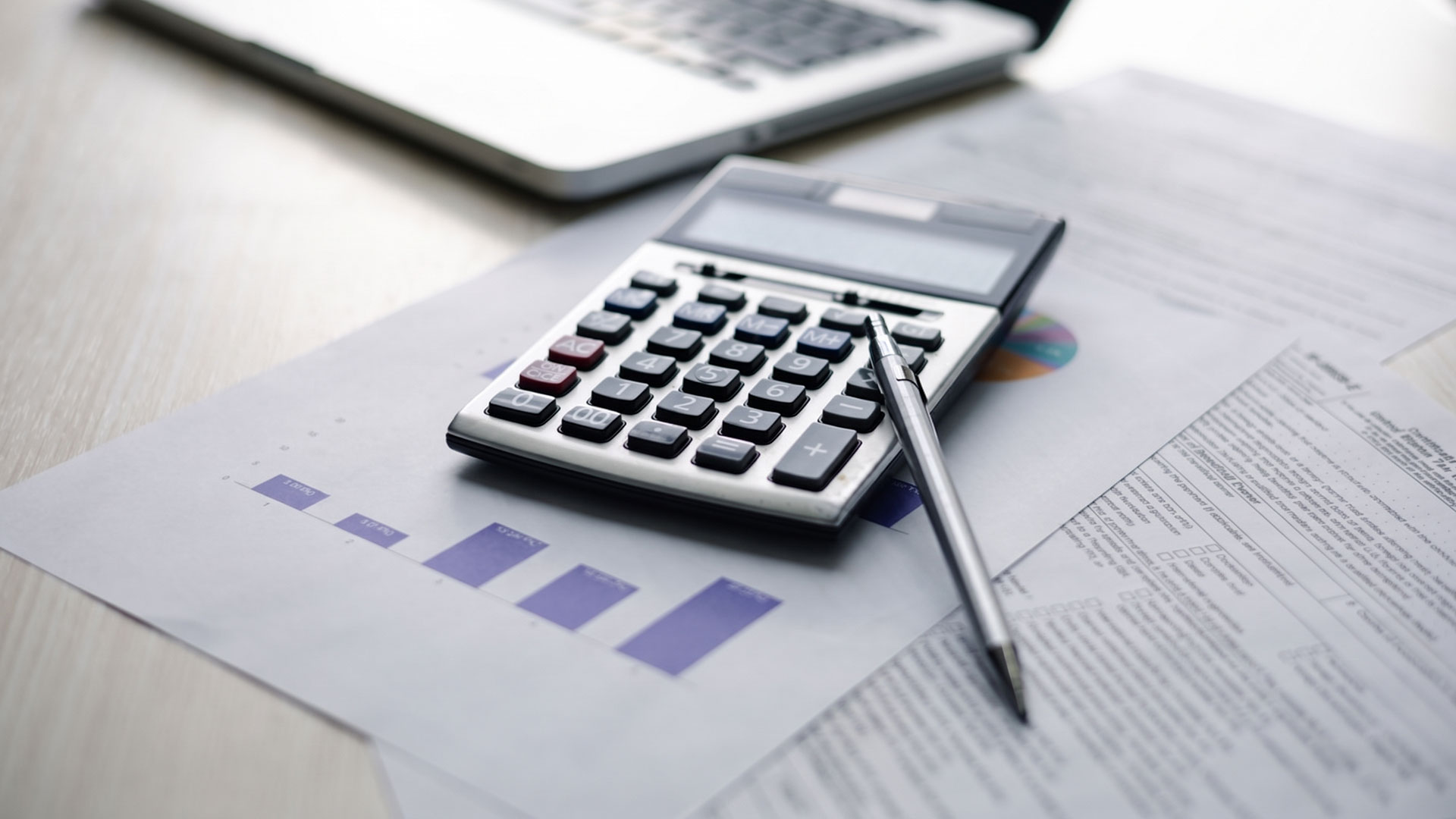 Calcolatrice e penna su documenti per l'analisi della fiscalità di operazioni straordinarie d'impresa.
