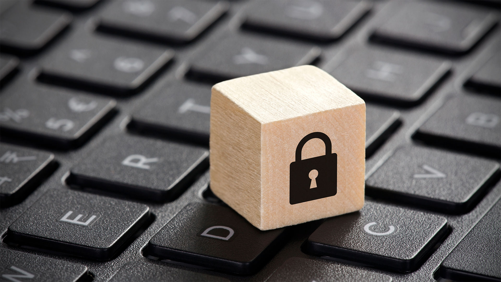 Blocco di legno con icona di un lucchetto poggiato su una tastiera di computer, simbolo di protezione dei dati